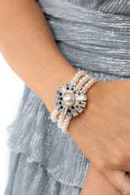 Load image into Gallery viewer, Strung along elastic stretchy bands, three bands of pearls wrap around the wrist. Featured atop the pearly collection, sleek metal bars flare out from a mesmerizing pearl center, creating a stacked blue and white rhinestone-encrusted fringe of fanning frames. A trio of emerald-cut white gem bars are sprinkled across the dazzling display for a sassy finish.