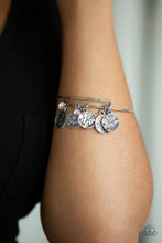 Load image into Gallery viewer, A skinny silver wire is adorned by a collection of small silver charms. Each charm features a floral design and one of the many titles that women hold throughout their lives. Words include, “Mother”, “Grandmother”, “Sister”, Daughter”, and “Friend.” A small white rhinestone is nestled among the silver charms, while a larger one is placed as an end cap on the spiraling wire, both adding sparkling accents to the piece. The coil can be expanded to accommodate a larger wrist. Sold as one individual bracelet.