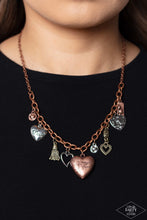 Load image into Gallery viewer, An array of brass, copper, and silver heart charms trickle from a section of bold copper chain, creating a whimsical fringe below the collar. The largest heart charm is inscribed with the phrase, “With all my heart” on one side and a short bible verse on the other that reads, "Love the lord thy God with all your heart. Luke 10:27.” Features an adjustable clasp closure. Sold as one individual necklace. Includes one pair of matching earrings.
