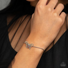 Load image into Gallery viewer, A deceptively simple silver butterfly charm glides along a silver snake chain for a whimsical flair along the wrist. Dainty, pink rhinestones, brushed in a UV shimmer, encrust along the butterfly's body, creating an understated shimmer, while intricate, airy wings fold out from the sparkle, adding a 3D effect to the design. Features an adjustable sliding knot closure. Due to its prismatic palette, color may vary. Sold as one individual bracelet.