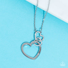 Load image into Gallery viewer, A silver heart engraved with the word "Grandma," dangles from two smaller hearts at the bottom of a lengthened silver chain. The first heart is accented with sparkly white rhinestones creating an affectionately sentimental pendant. Features an adjustable clasp closure. Sold as one individual necklace. Includes one pair of matching earrings.