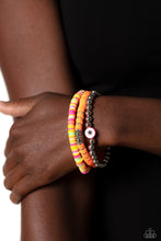 Load image into Gallery viewer, Varying in colorful shades, orange, pink, green, white, and yellow rubber discs pair with shiny silver beads and silver accents creating colorful layers across the wrist. Featured on the silver-beaded bracelet, a rubber shape with an eye-like design contributes an additional shade of pink to the design. Sold as one set of three bracelets.