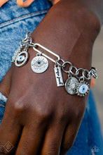 Load image into Gallery viewer, A harmonious compilation of charms, featuring tranquil shades of blue and accents of black, wrap around the wrist on a handcrafted chain. Elongated paperclip links and oversized jump rings interlock in a homespun fashion, showcasing the variety of charms that include a rhinestone-dusted sunburst and sunburst pendant, an eye with tactile silver eyelashes, a rectangular pendant stamped with the phrase good vibes and an ornate, rhinestone-encrusted eye charm. Features an adjustable clasp closure.
