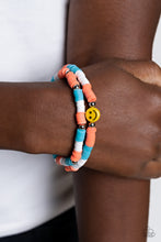 Load image into Gallery viewer, Coral, blue, and white rubber discs combine with sporadically placed silver beads to provide a vibrant pop of color along the wrist. Meeting in the center of one of the multi-shaded bracelets, a yellow bead with a smiley face, featuring stars for eyes, rests for a youthful finish. Sold as one set of two bracelets.