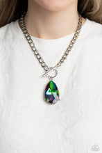 Load image into Gallery viewer, Featuring an elegant lariat closure, an oversized, faceted, stellar UV shimmery teardrop gem, encased in an elevated pronged silver frame cascades from the bottom of a silver curb chain in a whimsical fashion. Dainty hematite rhinestones are encrusted along the ring as the lariat closure loops through for a touch of edgy shimmer to the exaggerated sparkly design. Due to its prismatic palette, color may vary. Sold as one individual necklace. Includes one pair of matching earrings.