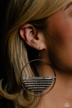 Load image into Gallery viewer, A curtain of white rhinestones is stretched between the edges of a skinny, oversized gunmetal hoop, creating a shimmering display. The rhinestones taper towards the center as they sway and cascade, adding sparkly movement for a fierce industrial finish. Earring attaches to a standard fishhook fitting. Sold as one pair of earrings.