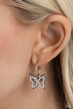Load image into Gallery viewer, A small, skinny, shiny silver hoop curves around the ear in a timeless fashion. A shiny silver ball is affixed to the end of the hoop, reminiscent of a barbell fitting. A white rhinestone-encrusted butterfly frame, layered in front of a shiny silver airy butterfly frame, slides along the curvature of the hoop, adding a whimsical hint of shimmery movement. Earring attaches to a standard post fitting. Hoop measures approximately 1/2" in diameter. Sold as one pair of hoop earrings.