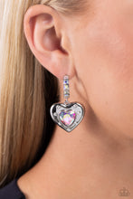Load image into Gallery viewer, Featuring an iridescent shimmer, an iridescent heart gem is pressed into an antiqued silver heart frame adorned in white rhinestones. The antiqued heart sways from the bottom of a thick silver hoop encrusted in square iridescent gems resulting in a whimsical fashion. Earring attaches to a standard post fitting. Hoop measures approximately 3/4" in diameter. Due to its prismatic palette, color may vary. Sold as one pair of hoop earrings.