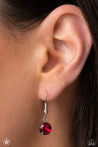 A single fuchsia rhinestone sparkles brilliantly at the bottom of a silver fish hook earring.