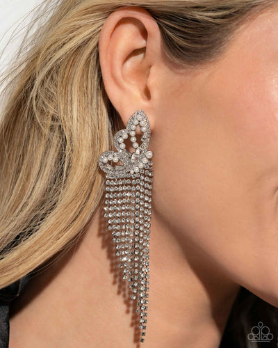 Glassy white rhinestones, dainty white pearls, and white emerald-cut gems are encrusted along the front of an airy silver butterfly frame, creating a whimsical centerpiece. Staggered rows of white rhinestones pressed in delicate silver square fittings cascade from the sparkly centerpiece, seemingly lifting the butterfly off to its glitzy flight. Earring attaches to a standard post fitting. Sold as one pair of post earrings.