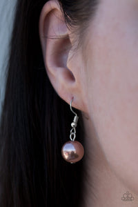Tan pearl hanging from a silver fish hook earring.