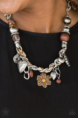 Brown and ivory cording is braided through a chunky silver chain. A unique variety of charms decorate the Blockbuster piece, including a delicate flower and a heart inscribed with the phrase 