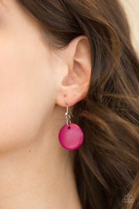Pink wood disc hanging from a silver fish hook earring.