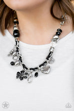 Load image into Gallery viewer, Black and ivory cording is braided through a chunky silver chain. A unique variety of charms decorate the Blockbuster piece, including a delicate flower and a heart. Heart is inscribed with the phrase &quot;With All My Heart&quot; on one side and a short bible verse on the other that reads, &quot;Love the Lord thy God with all your heart. Luke 10:27.&quot; Features an adjustable clasp closure. Sold as one individual necklace. Includes one pair of matching earrings.
