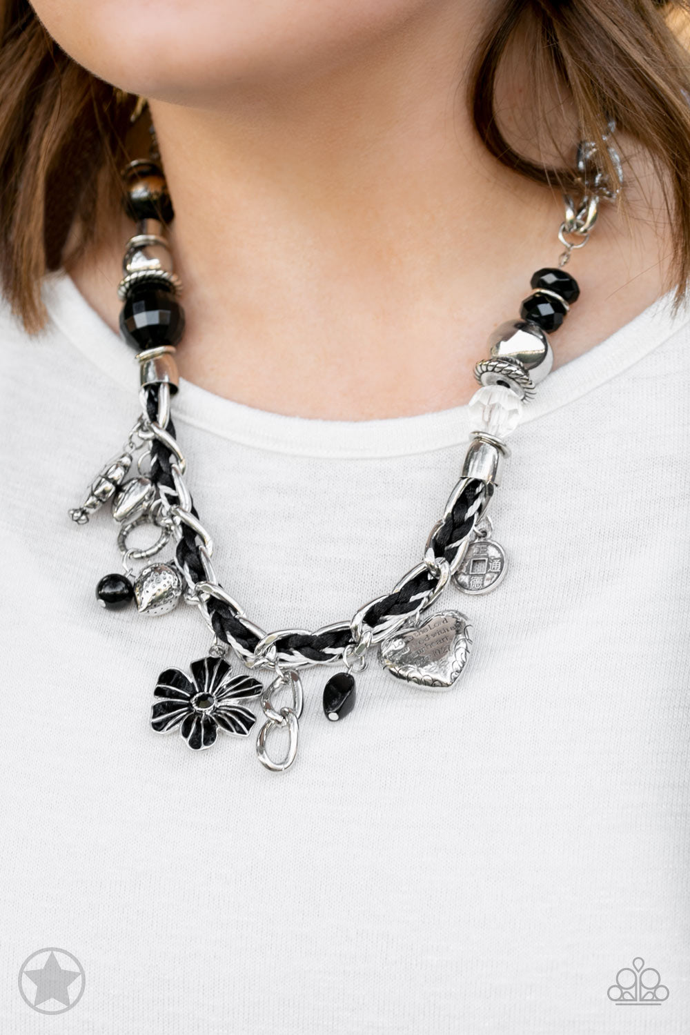 Black and ivory cording is braided through a chunky silver chain. A unique variety of charms decorate the Blockbuster piece, including a delicate flower and a heart. Heart is inscribed with the phrase 
