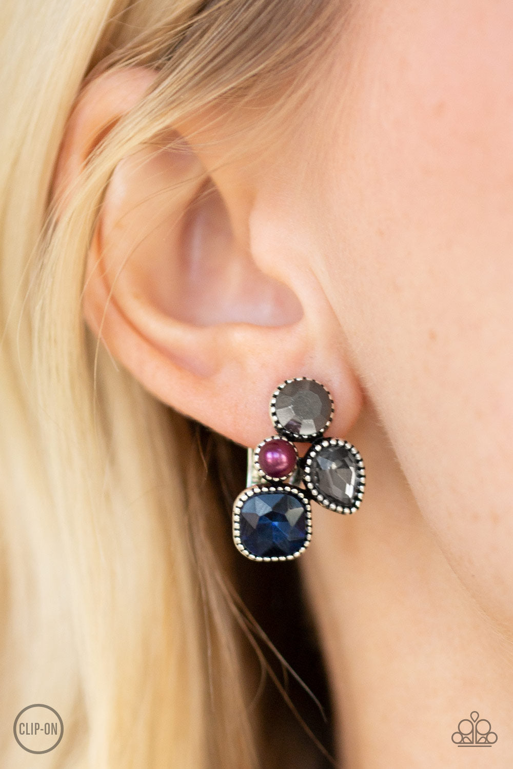 Infused with a dainty purple pearl, mismatched blue, smoky, and hematite rhinestones coalesce into a glittery frame. Earring attaches to a standard clip-on fitting. Sold as one pair of clip-on earrings.