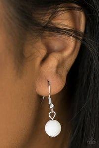 White bead handing from a silver fish hook earring.