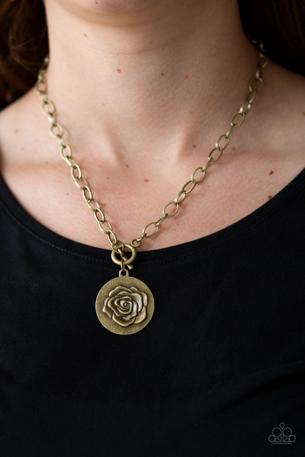 Embossed in a whimsical rosebud pattern, a shimmery brass frame swings below the collar for a casual look. Features a toggle closure. Sold as one individual necklace. Includes one pair of matching earrings.