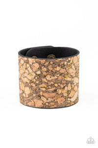 Pieces of cork have been plastered across the front of a black leather band, creating an earthy look around the wrist. Specks of glittery brass accents are sprinkled across the front for a flashy finish. Features an adjustable snap closure.  Sold as one individual bracelet.