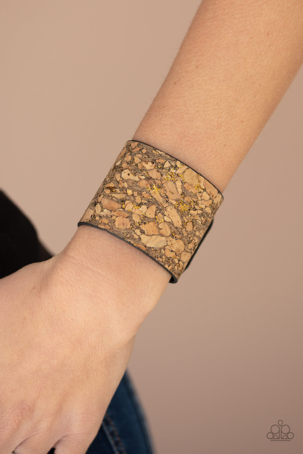 Pieces of cork have been plastered across the front of a black leather band, creating an earthy look around the wrist. Specks of glittery brass accents are sprinkled across the front for a flashy finish. Features an adjustable snap closure.  Sold as one individual bracelet.