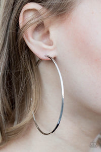 A skinny ribbon of silver curls into a bold hoop for a dramatic look. Earring attaches to a standard post fitting. Hoop measures 3” in diameter. Sold as one pair of hoop earrings.