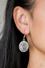 Load image into Gallery viewer, Embossed in a whimsical rosebud pattern, a shimmery silver frame swings from a silver fish hook earring.
