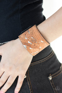 Pieces of cork have been plastered across the front of a shiny silver leather band, creating an earthy look around the wrist. Features an adjustable snap closure.  Sold as one individual bracelet.