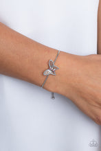 Load image into Gallery viewer, A deceptively simple silver butterfly charm glides along a silver snake chain for a whimsical flair along the wrist. Dainty, pink rhinestones, brushed in a UV shimmer, encrust along the butterfly&#39;s body, creating an understated shimmer, while intricate, airy wings fold out from the sparkle, adding a 3D effect to the design. Features an adjustable sliding knot closure. Due to its prismatic palette, color may vary.  Sold as one individual bracelet.
