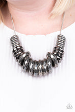 Load image into Gallery viewer, Gradually increasing in size, a collision of faceted silver and gunmetal rings slide along a classic silver chain below the collar for a bold industrial look. Features an adjustable clasp closure.  Sold as one individual necklace. Includes one pair of matching earrings.
