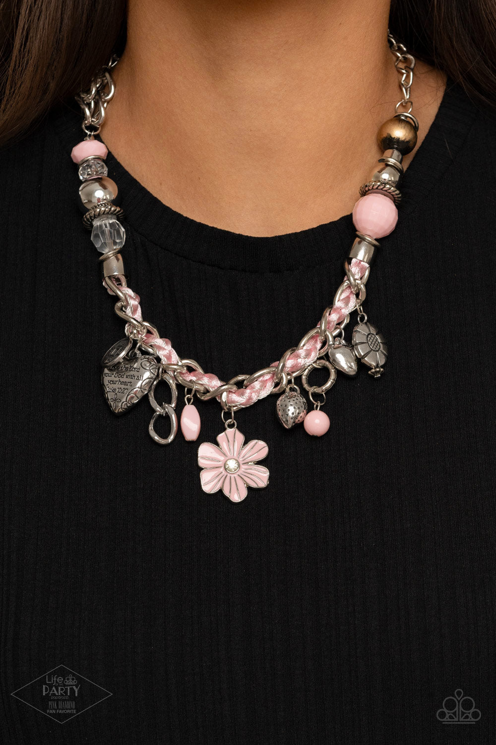 Pink cording is braided through a chunky silver chain. A unique variety of charms decorate the piece including a delicate flower and a heart inscribed with the phrase 