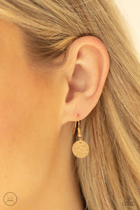 Gold hammered disc hanging from a gold fish hook earring.
