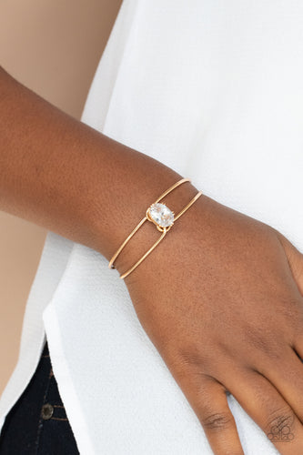 A dramatically oversized white rhinestone is fitted in place atop the center of a gold wire cuff, creating a jaw-dropping display around the wrist.  Sold as one individual bracelet.