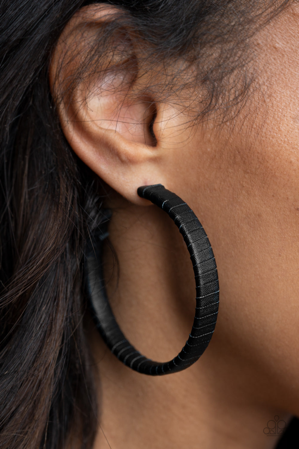 A black leather lace wraps around a thick silver hoop, creating an edgy display. Earring attaches to a standard post fitting. Hoop measures approximately 2 1/2