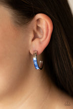 Load image into Gallery viewer, The front of a thick silver hoop is encrusted in glittery blue emerald cut rhinestones, creating a glamorous pop of color. Earring attaches to a standard post fitting. Hoop measures approximately 1&quot; in diameter.  Sold as one pair of hoop earrings.
