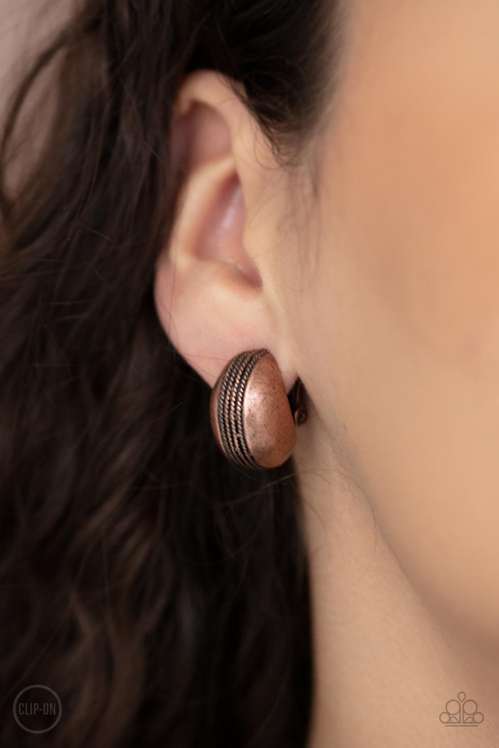The center of a round copper frame is embossed in textured columns, accentuating the frame's dainty curve. Earring attaches to a standard clip-on fitting.  Sold as one pair of clip-on earrings.