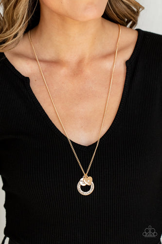 Dotted with a sparkly white rhinestone, a dainty gold heart joins a gold ring stamped in the biblical passage, 