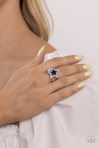 A star shaped blue gem is pressed into the center of a silver star dotted in blinding white rhinestones, creating a stellar centerpiece atop two white rhinestone encrusted silver bands. Features a stretchy band for a flexible fit.  Sold as one individual ring.