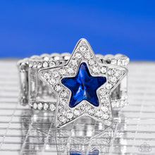 Load image into Gallery viewer, A star shaped blue gem is pressed into the center of a silver star dotted in blinding white rhinestones, creating a stellar centerpiece atop two white rhinestone encrusted silver bands. Features a stretchy band for a flexible fit.  Sold as one individual ring.
