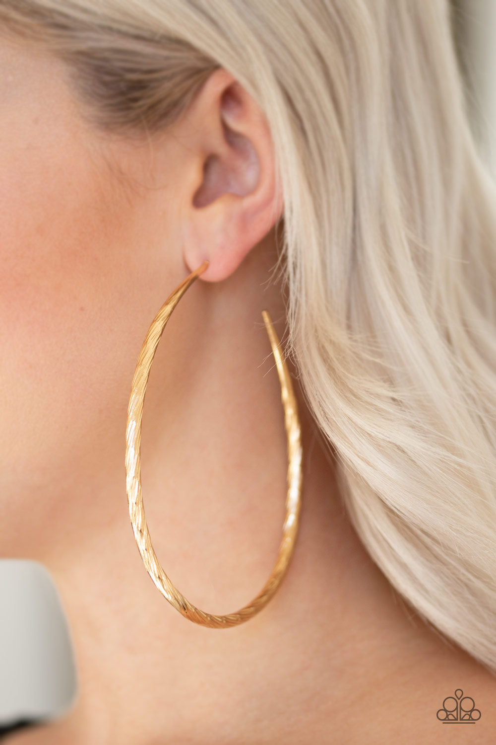 Etched in shimmer, a rippling gold bar bends into a dramatic asymmetrical hoop for a showstopping look. Earring attaches to a standard post fitting. Hoop measures 3