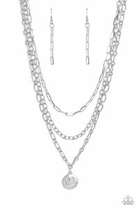 A trio of silver paperclip, classic, and oval link chains coalesces down the neckline for a monochromatic masterpiece. Strung on the lowermost oval link chain, a silver smiley face pendant, with a star mimicking a wink for one of its eyes, stands out and reflects light in every direction for a statement finish. Features an adjustable clasp closure.  Sold as one individual necklace. Includes one pair of matching earrings.
