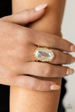 Load image into Gallery viewer, A dramatically oversized oval white gem adorns the center of a scalloped gold frame dusted in dainty white rhinestones, creating a commanding centerpiece atop the finger. Features a stretchy band for a flexible fit.  Sold as one individual ring.
