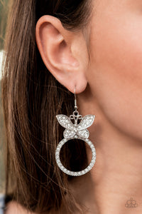 A white rhinestone encrusted silver butterfly flutters atop a silver ring dotted in matching white rhinestones, resulting in a dazzling statement piece. Earring attaches to a standard fishhook fitting.  Sold as one pair of earrings.
