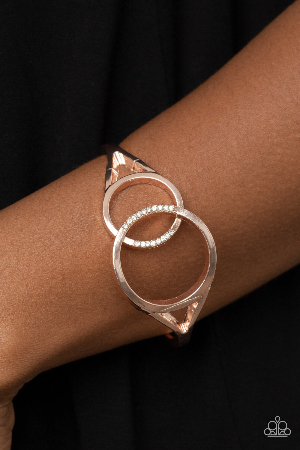 Encrusted in sections of glassy white rhinestones, two oversized rose gold rings delicately overlap across the center of the wrist, resulting in a timeless bangle-like bracelet around the wrist. Features a hinged closure.  Sold as one individual bracelet.