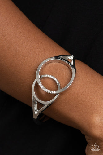 Encrusted in sections of glassy white rhinestones, two oversized silver rings delicately overlap across the center of the wrist, resulting in a timeless bangle-like bracelet around the wrist. Features a hinged closure.  Sold as one individual bracelet.