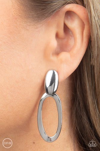 An asymmetrical silver oval hinges from the bottom of a spherical silver oval fitting, resulting in a radiant lure. Earring attaches to a standard clip-on fitting.  Sold as one pair of clip-on earrings.