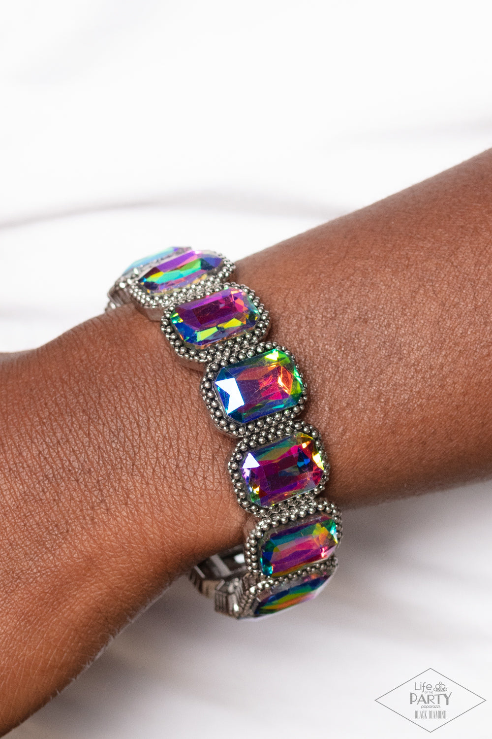Oversized emerald style oil spill gems are encased in antiqued studded frames that are threaded along stretchy bands around the wrist, creating a smoldering centerpiece. Due to its prismatic palette, color may vary.  Sold as one individual bracelet.