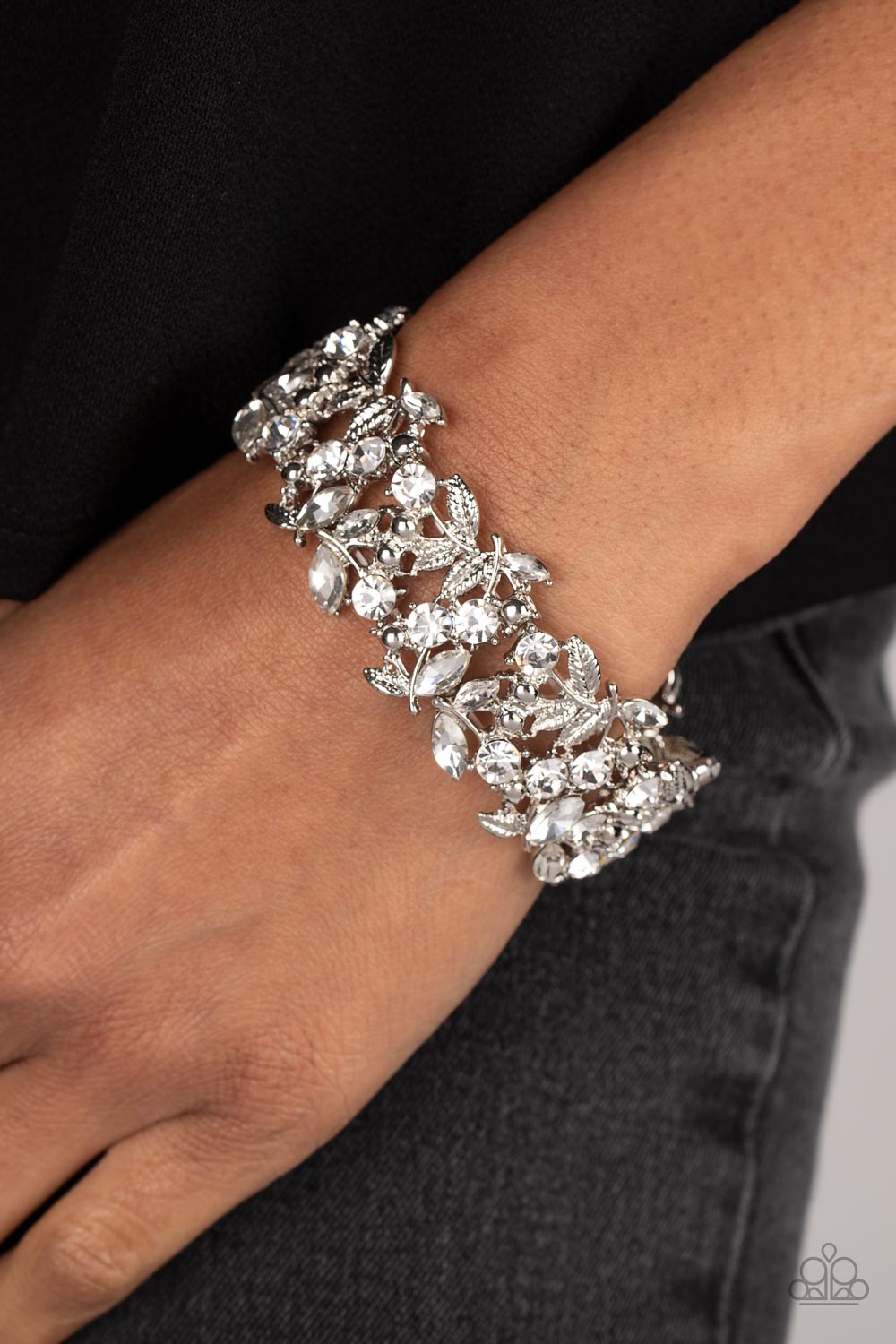 Round and marquise-cut white gems intertwine around polished silver studs and ornate feather-like details in a glitzy pattern. The textured, glittery display is threaded along elastic stretchy bands for a whimsical finish.  Sold as one individual bracelet.