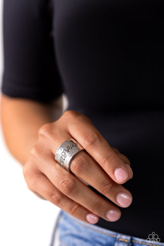 Across a wide silver band with a hammered sheen, the phrase 