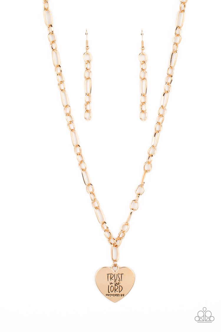 Dangling from a gold figaro chain, a charming heart pendant swings. Stamped upon the shiny surface, the phrase 