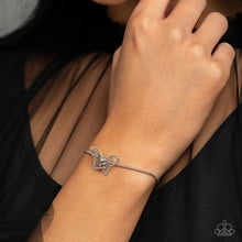 Load image into Gallery viewer, A deceptively simple silver butterfly charm glides along a silver snake chain for a whimsical flair along the wrist. Dainty, pink rhinestones, brushed in a UV shimmer, encrust along the butterfly&#39;s body, creating an understated shimmer, while intricate, airy wings fold out from the sparkle, adding a 3D effect to the design. Features an adjustable sliding knot closure. Due to its prismatic palette, color may vary.  Sold as one individual bracelet.
